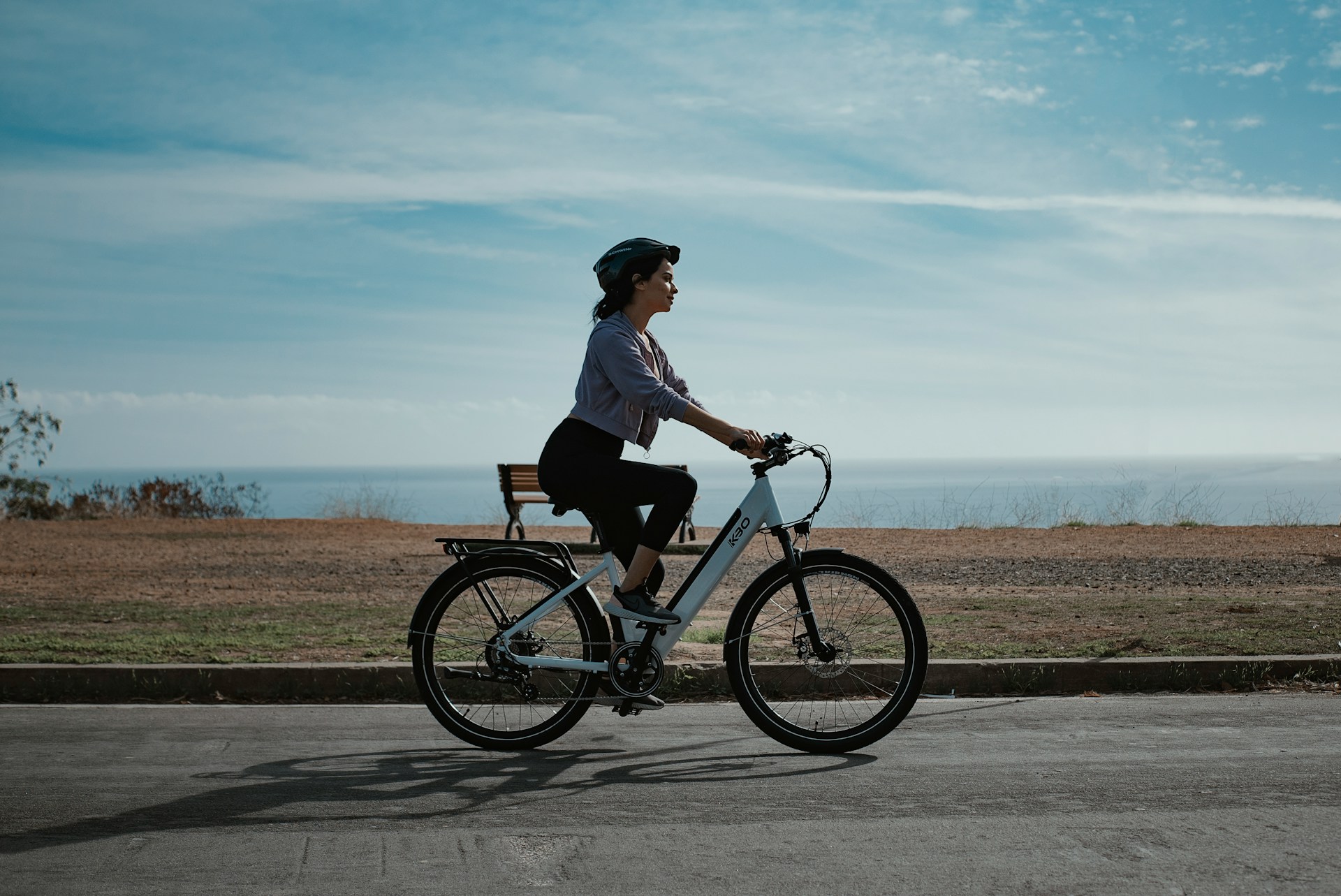 A woman rides a bike on a street by the ocean