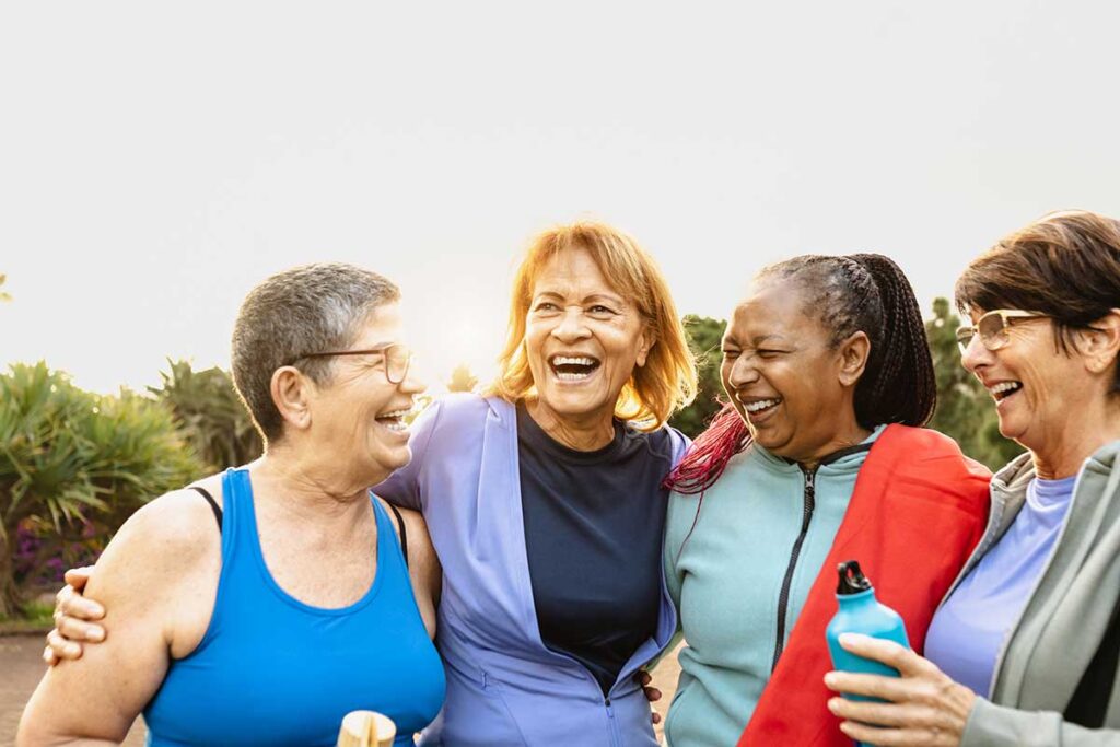 A diverse group of four older woman come together for a group hug after a great outdoor workout